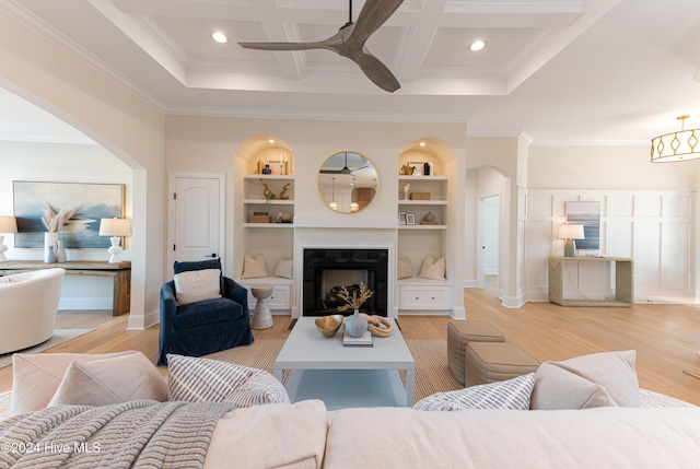 living room featuring coffered ceiling, crown molding, built in features, light wood-type flooring, and beamed ceiling