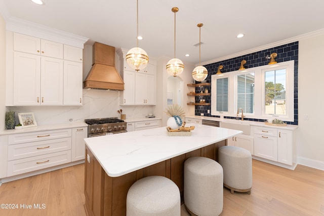 kitchen with appliances with stainless steel finishes, premium range hood, pendant lighting, white cabinets, and a center island