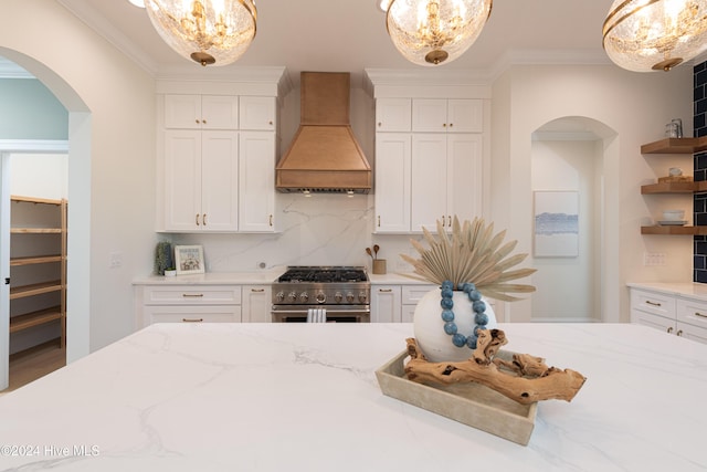 kitchen with premium range hood, white cabinets, high end stove, tasteful backsplash, and decorative light fixtures