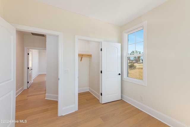 unfurnished bedroom with a spacious closet, a closet, and light hardwood / wood-style floors