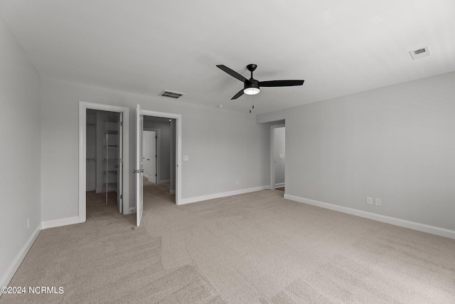 unfurnished bedroom featuring light colored carpet, ceiling fan, a walk in closet, and a closet