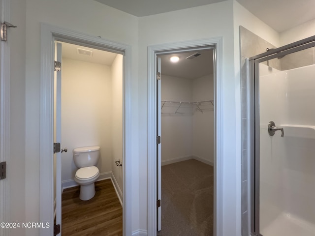 bathroom featuring a shower stall, a walk in closet, baseboards, toilet, and visible vents