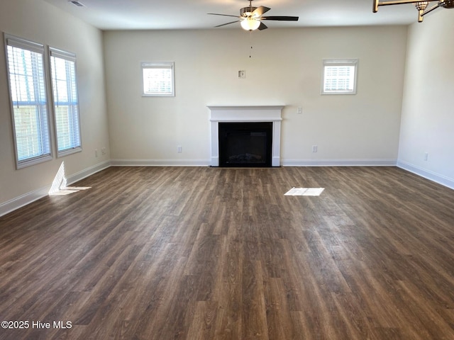 unfurnished living room with a fireplace, a healthy amount of sunlight, a ceiling fan, and dark wood-style floors