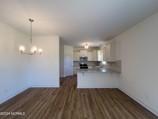 kitchen with light stone counters, an inviting chandelier, stainless steel appliances, a peninsula, and dark wood-style floors