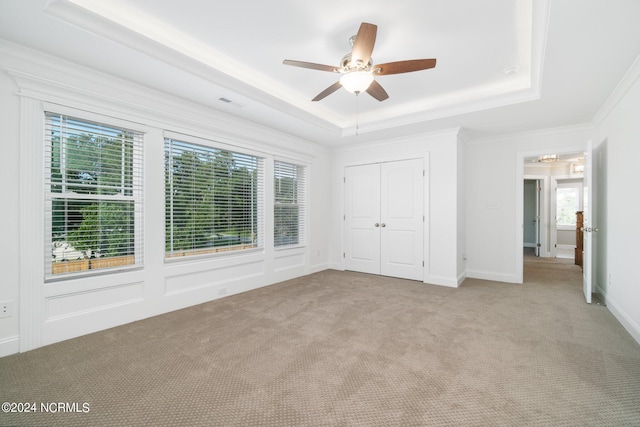 unfurnished bedroom with light carpet, ornamental molding, ceiling fan, a closet, and a tray ceiling