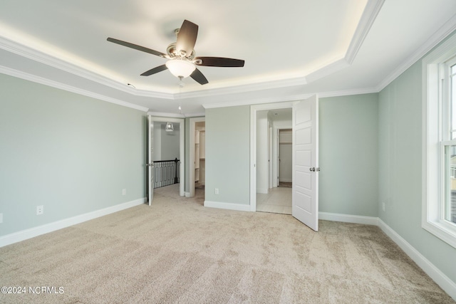 unfurnished bedroom with crown molding, ceiling fan, light colored carpet, and a raised ceiling