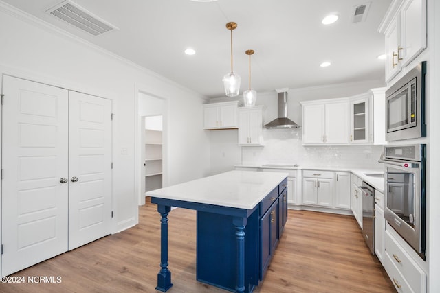 kitchen featuring wall chimney range hood, white cabinetry, blue cabinetry, pendant lighting, and stainless steel appliances