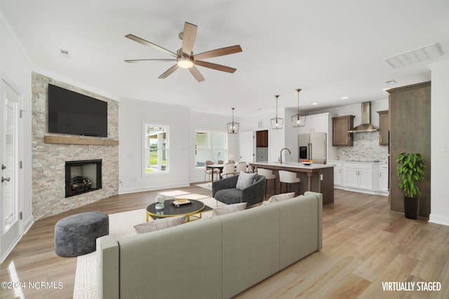 living room with a fireplace, light hardwood / wood-style flooring, ornamental molding, sink, and ceiling fan