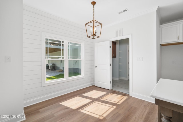 unfurnished dining area featuring light wood-type flooring, ornamental molding, a chandelier, and wood walls