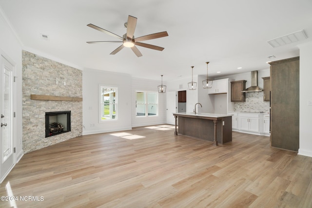 kitchen featuring a center island with sink, ceiling fan, wall chimney range hood, and light hardwood / wood-style floors