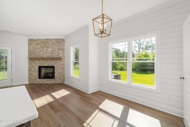 unfurnished living room featuring dark hardwood / wood-style flooring, a wealth of natural light, a notable chandelier, and a stone fireplace