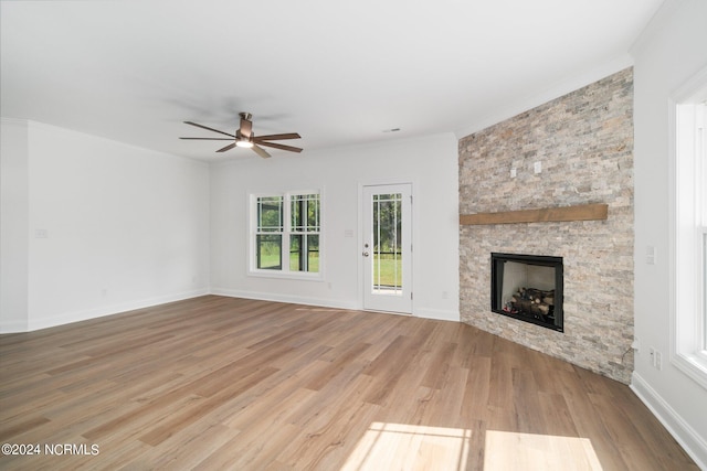 unfurnished living room with crown molding, hardwood / wood-style floors, ceiling fan, and a stone fireplace