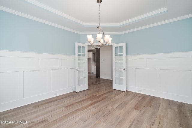 unfurnished dining area with a tray ceiling, french doors, a wainscoted wall, a chandelier, and light wood-type flooring