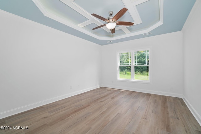 empty room featuring light wood-type flooring, coffered ceiling, a tray ceiling, ceiling fan, and ornamental molding