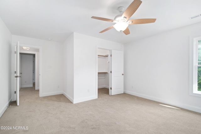 unfurnished bedroom with a closet, ceiling fan, a spacious closet, and light carpet