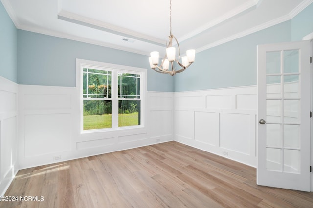 unfurnished room with crown molding, a raised ceiling, an inviting chandelier, and light hardwood / wood-style floors