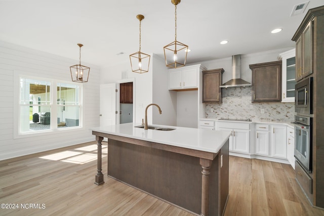 kitchen with wall chimney exhaust hood, light hardwood / wood-style floors, an island with sink, stainless steel appliances, and sink