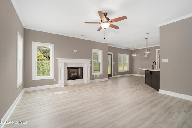 unfurnished living room with a wealth of natural light, ceiling fan with notable chandelier, light hardwood / wood-style floors, and ornamental molding