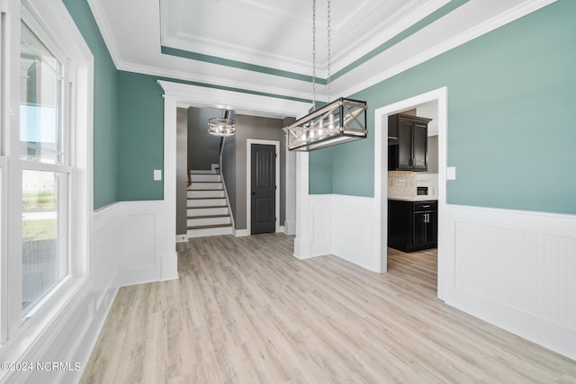 unfurnished room featuring light wood-style floors, stairs, wainscoting, a raised ceiling, and crown molding