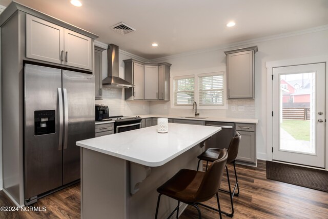 kitchen featuring a kitchen bar, sink, a kitchen island, stainless steel appliances, and wall chimney range hood