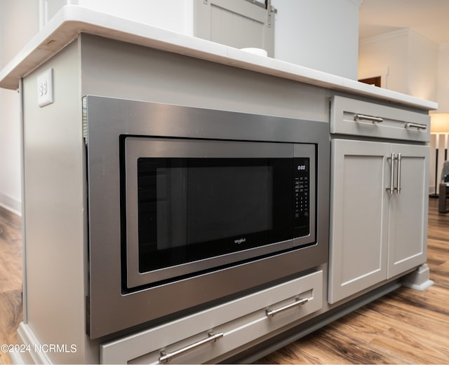 interior details featuring stainless steel microwave, ornamental molding, and light hardwood / wood-style flooring