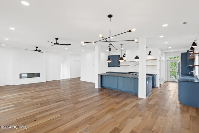 unfurnished living room featuring light hardwood / wood-style floors, sink, a fireplace, and ceiling fan with notable chandelier