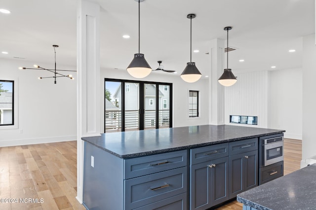 kitchen with dark stone counters, decorative light fixtures, wall oven, and light wood-type flooring