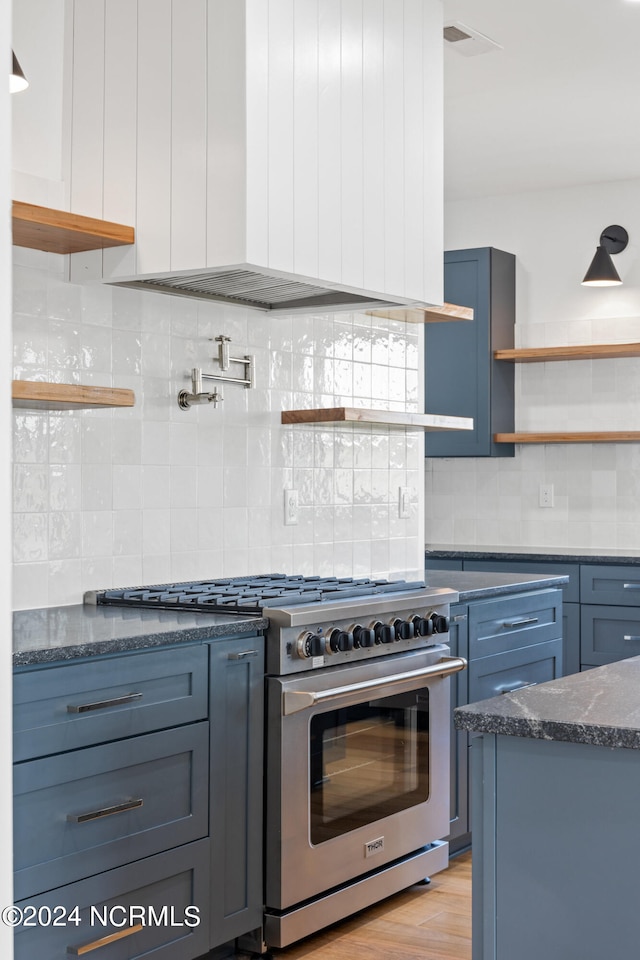 kitchen with decorative backsplash, designer stove, dark stone counters, and light wood-type flooring