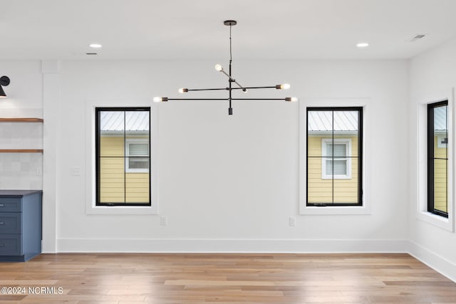 unfurnished dining area featuring a notable chandelier, a wealth of natural light, and light wood-type flooring