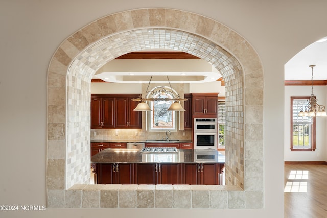 kitchen with decorative backsplash, light hardwood / wood-style flooring, beamed ceiling, pendant lighting, and stainless steel appliances