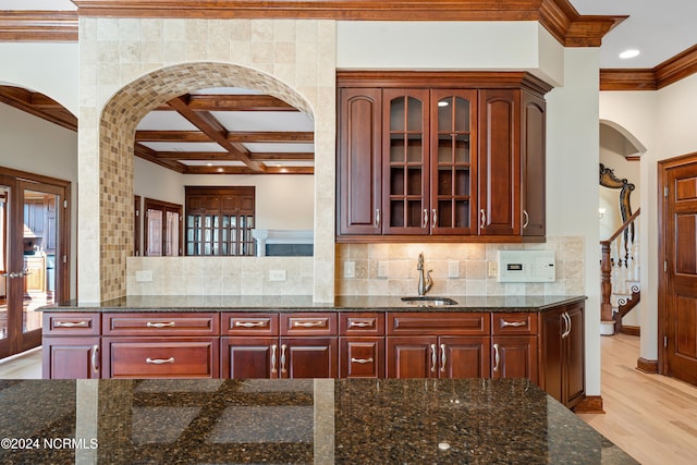 kitchen with tasteful backsplash, sink, coffered ceiling, dark stone countertops, and light hardwood / wood-style flooring