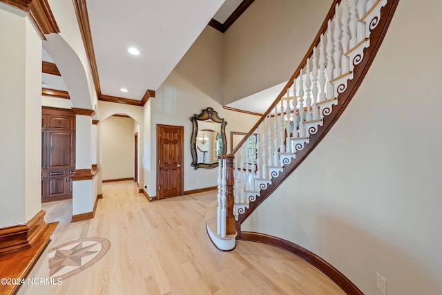 entryway featuring light hardwood / wood-style floors, crown molding, and a high ceiling