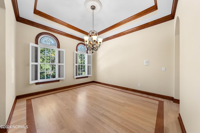 spare room with an inviting chandelier, crown molding, light wood-type flooring, and a raised ceiling