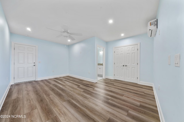 empty room with a wall mounted AC, light wood-type flooring, and ceiling fan