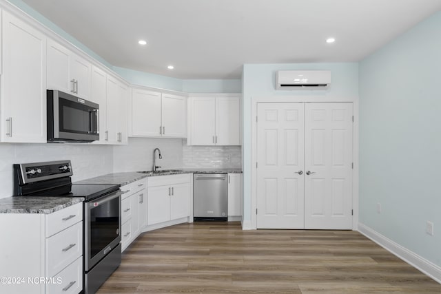 kitchen featuring appliances with stainless steel finishes, white cabinetry, hardwood / wood-style flooring, a wall mounted air conditioner, and sink