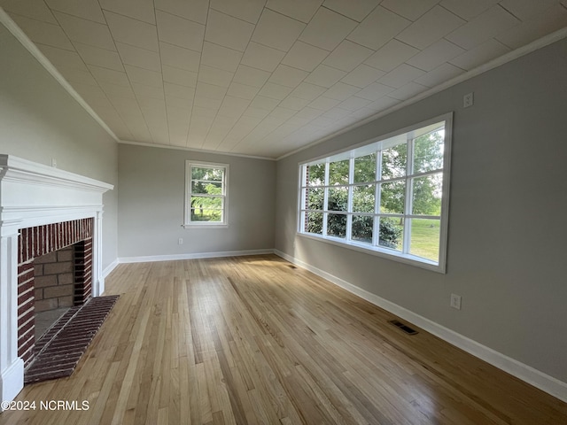 unfurnished living room with a brick fireplace, ornamental molding, and light hardwood / wood-style floors