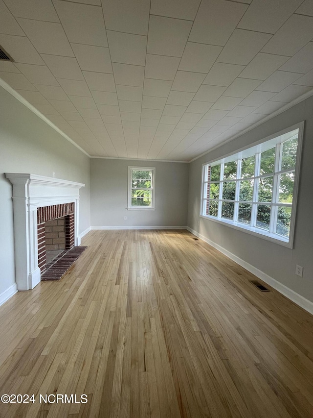 unfurnished living room featuring ornamental molding, light hardwood / wood-style floors, and a brick fireplace