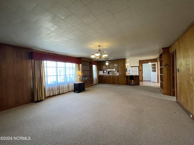 unfurnished living room featuring light colored carpet, a chandelier, and wood walls