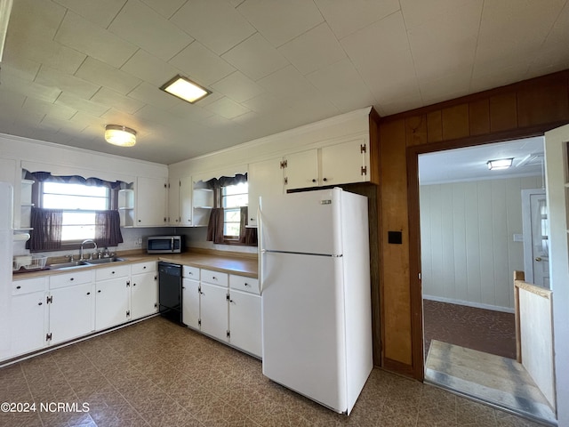 kitchen featuring wooden walls, dishwasher, sink, white cabinets, and white fridge