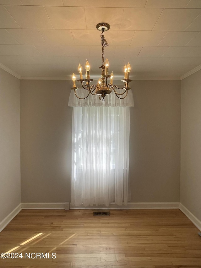 spare room with crown molding, hardwood / wood-style floors, and a chandelier