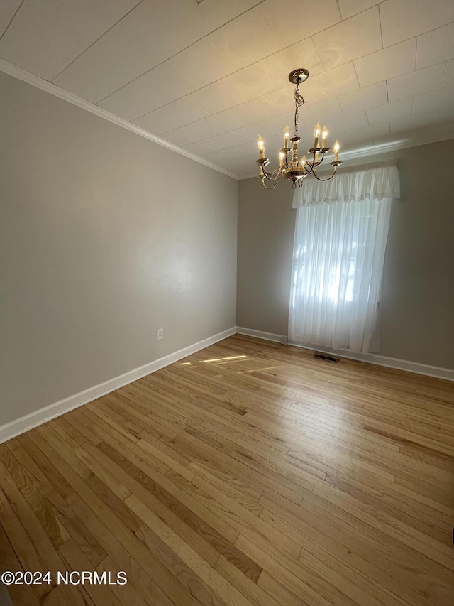 spare room with a notable chandelier, crown molding, and wood-type flooring