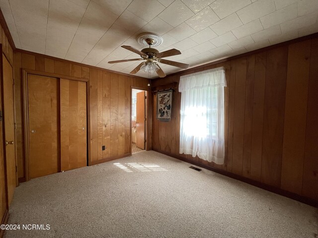 unfurnished bedroom with ceiling fan, carpet flooring, and wood walls