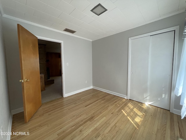 unfurnished bedroom with crown molding, light hardwood / wood-style floors, and a closet