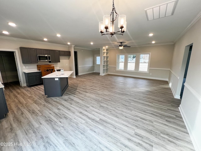 kitchen with light wood-type flooring, ornamental molding, ceiling fan with notable chandelier, a center island, and hanging light fixtures