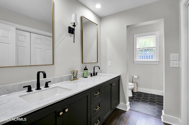 bathroom featuring toilet, double vanity, baseboards, and a sink