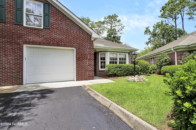 traditional home featuring aphalt driveway, brick siding, roof with shingles, a front yard, and a garage