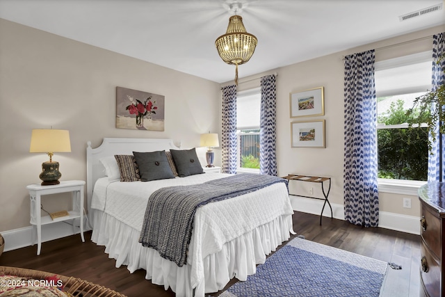 bedroom with an inviting chandelier, wood finished floors, visible vents, and baseboards