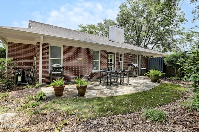 rear view of house with a patio area, brick siding, fence, and a chimney