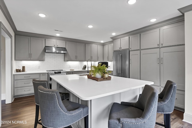 kitchen featuring premium appliances, dark wood-style floors, a breakfast bar area, gray cabinetry, and under cabinet range hood