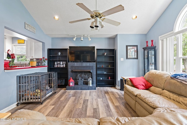 living room with light hardwood / wood-style flooring, vaulted ceiling, a tile fireplace, a textured ceiling, and ceiling fan